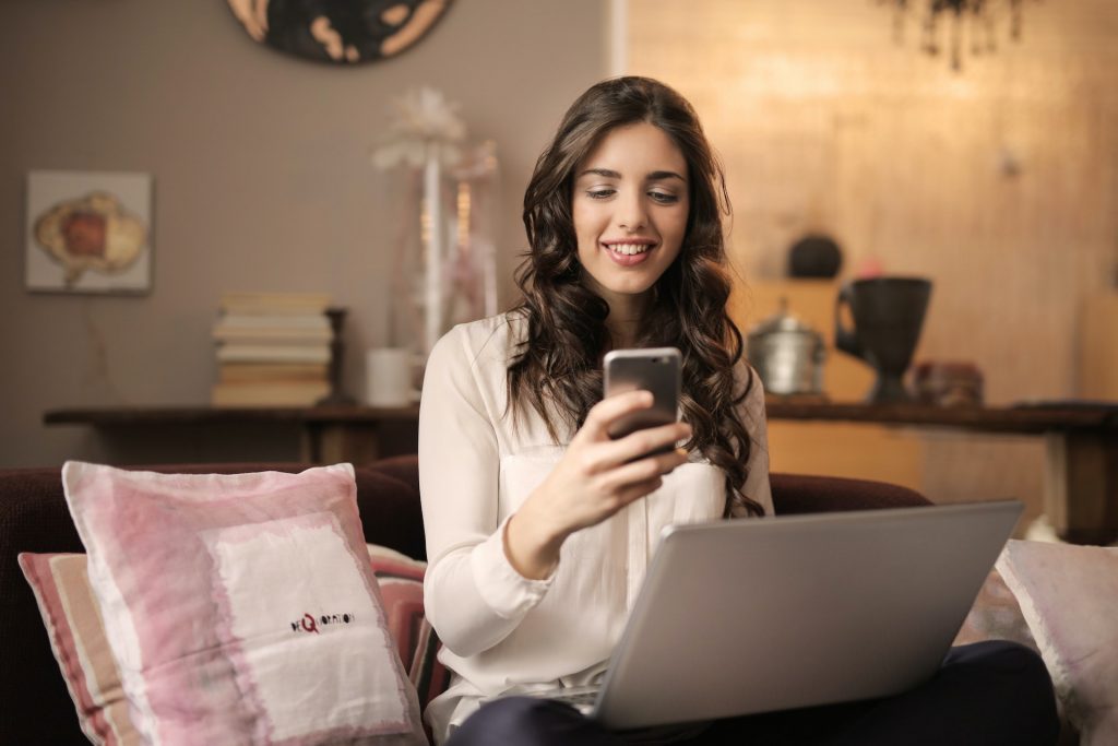 woman on her computer viewing something she likes on her phone